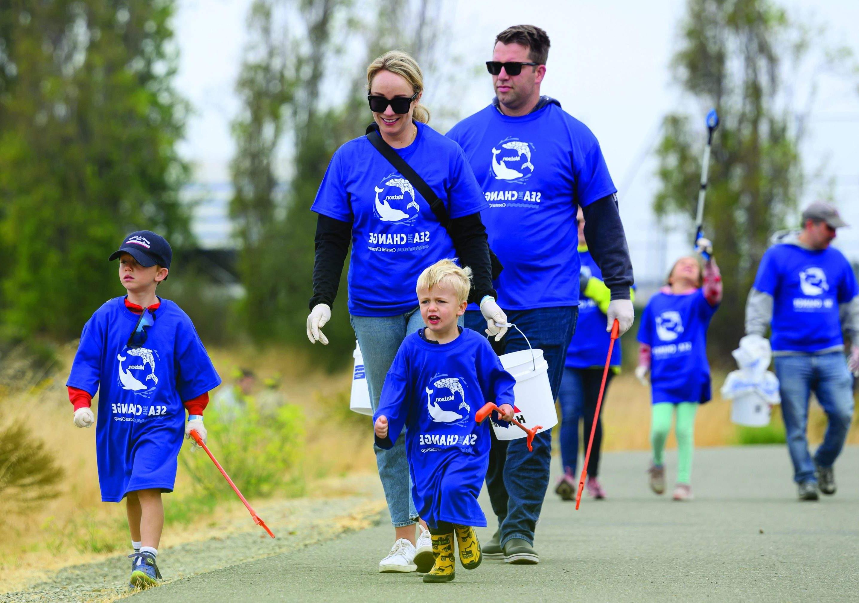 Family with two young boys wearing oversized, blue 澳博体育app下载 "Sea The Change" t-shirts walk to the clean-up site with grabbers and buckets.