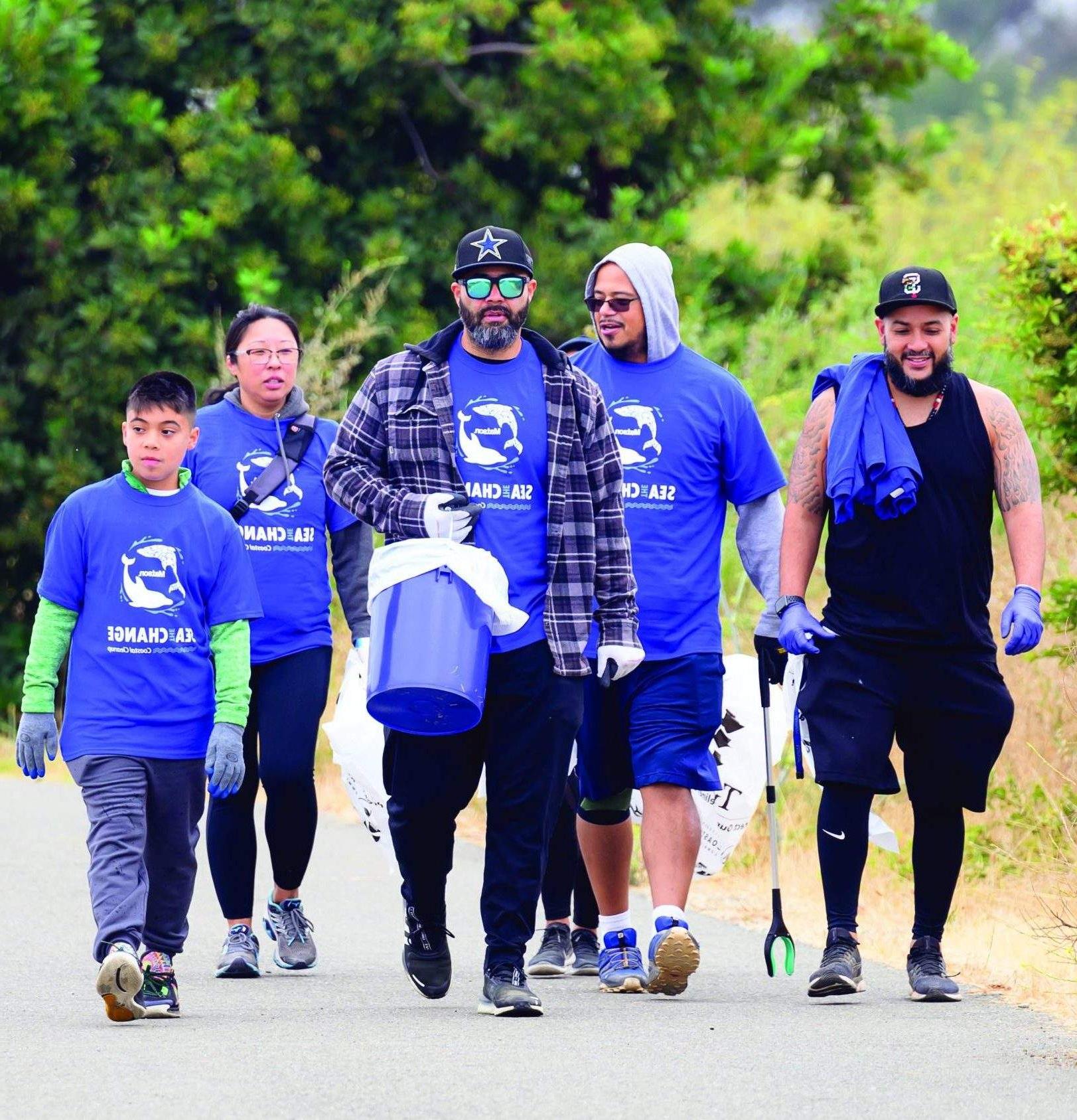 Group of volunteers wearing blue 澳博体育app下载 "Sea The Change" t-shirts and equipped with grabbers, bags and a bucket, walk to the clean-up area.